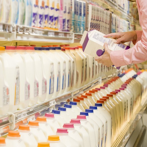 Customer inspecting health info on back of milk carton in supermarket