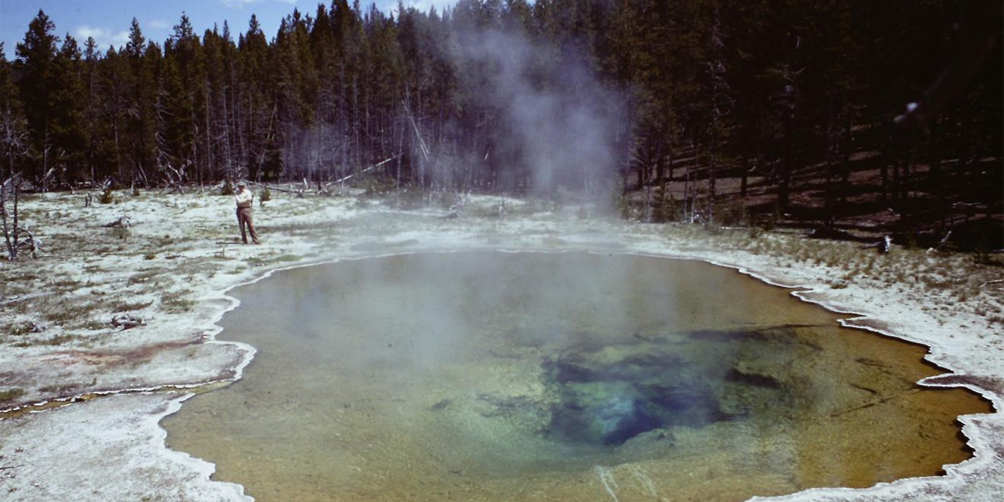 Mushroom Pool, in the Lower Geyser Basin of Yellowstone National Park, as it looked in June 23, 1967. The sample that would be the source of Thermus aquaticus strain YT-1 came from this hot spring. Pictured is Thomas Brock standing near the edge of the pool. Image from the self-published "A Scientist in Yellowstone National Park" (Brock, 2017).