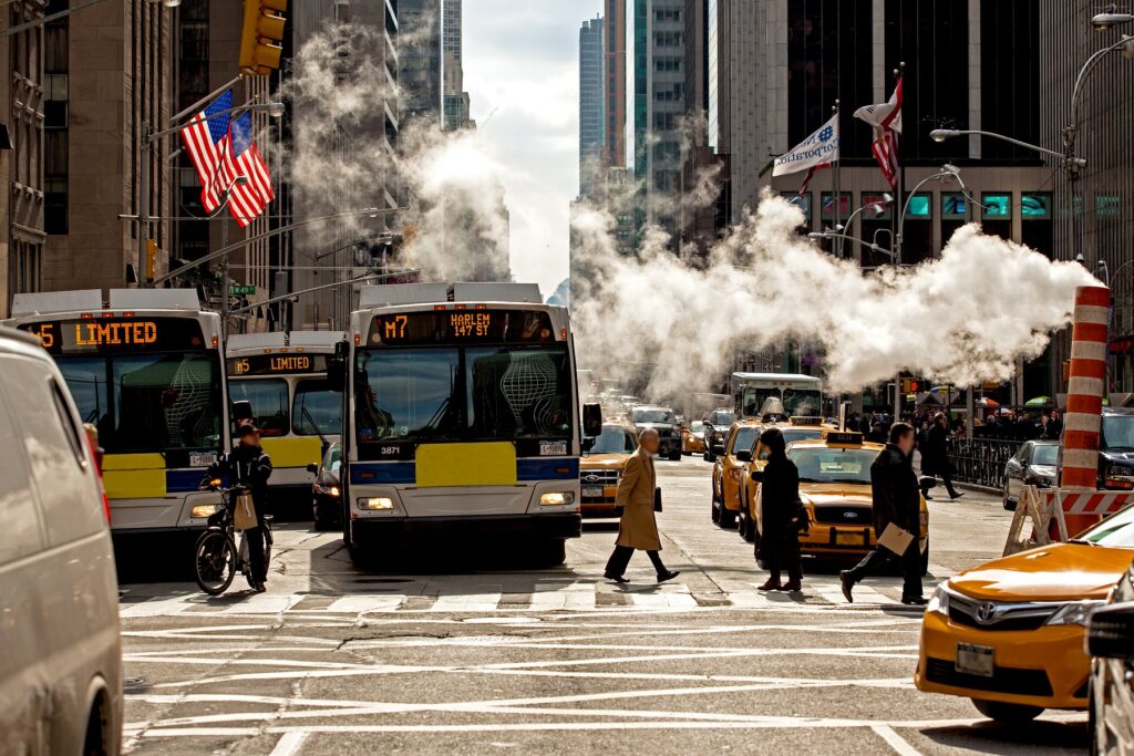 Construction exhaust floating across busy Manhattan street, with buses and taxis
